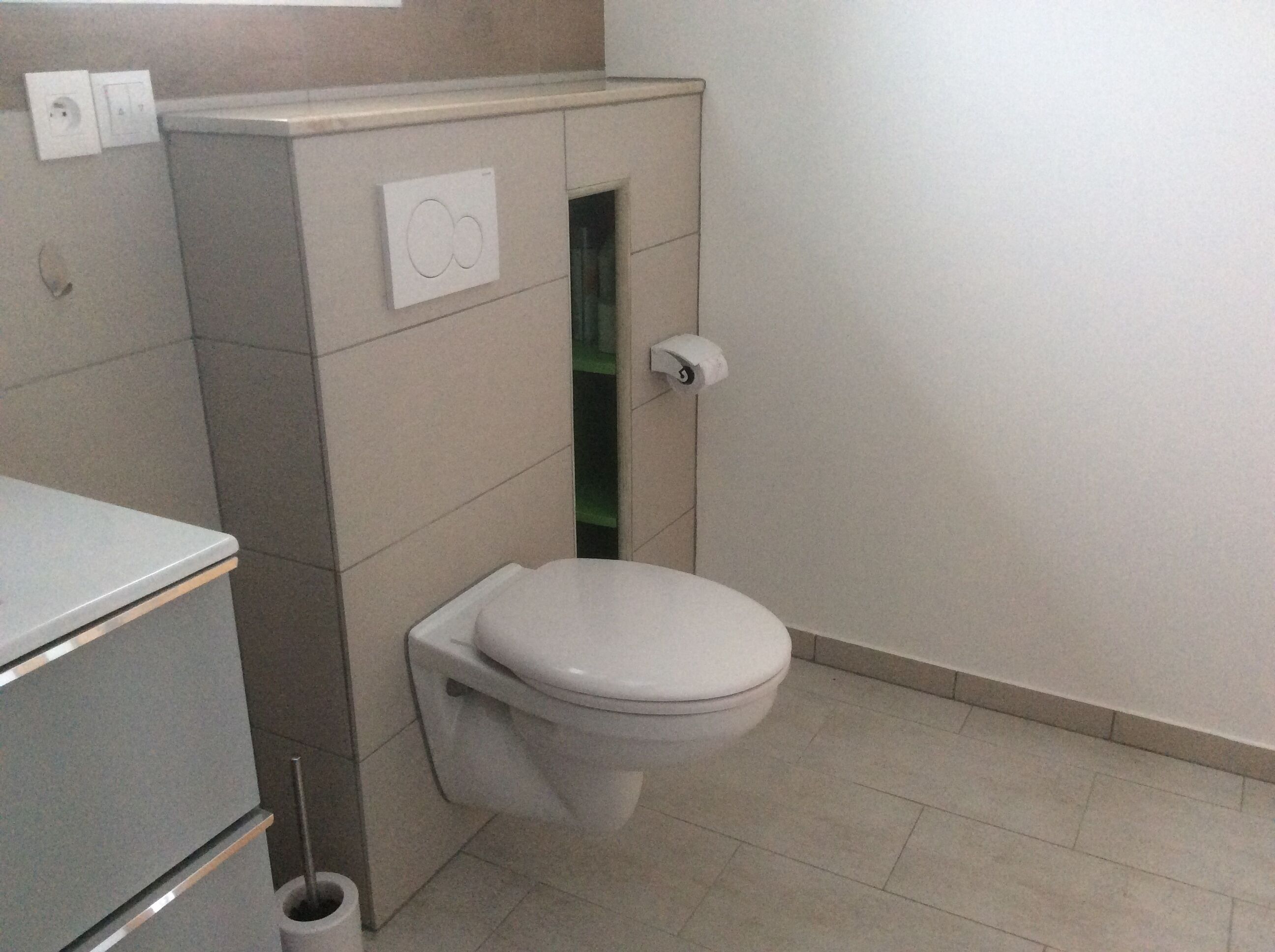 Un baño pequeño con inodoro, un cubo de basura y un enchufe en la pared.