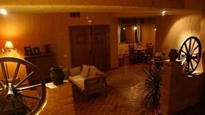 A cozy room with a brick floor, a wooden sofa, a dining table with chairs, and a large wooden wheel. - Eras de Pantrillar Rural House (full rental) for 10 people (Ciruelas)