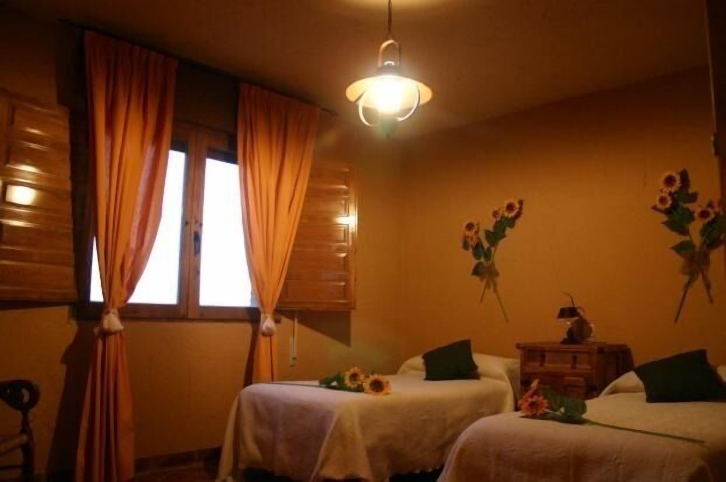 Una habitación con dos camas, cabecero de madera, mesita de noche y lámpara de pared.