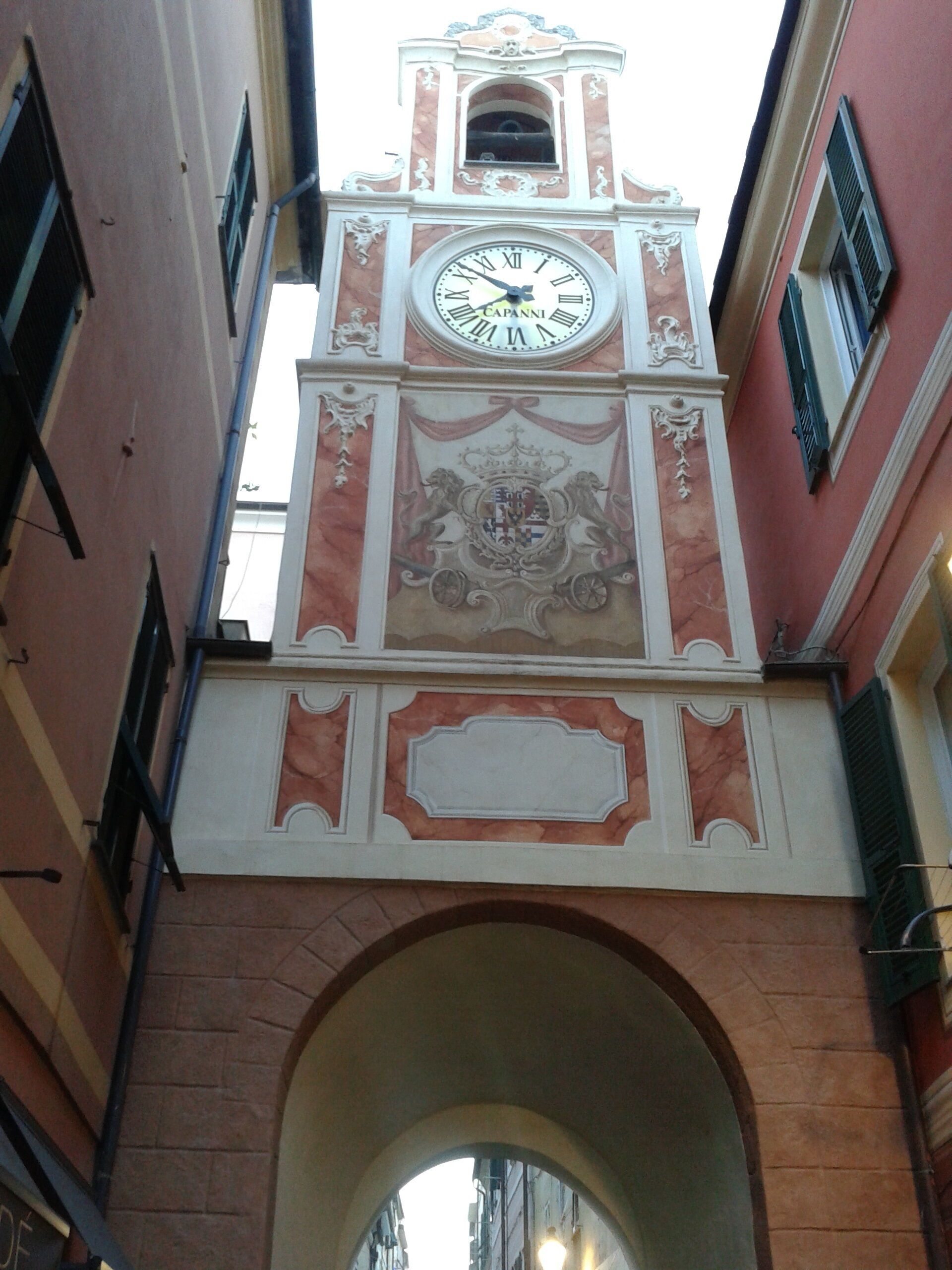 Una torre de reloj con esfera horaria, detalles arquitectónicos ornamentados y un arco de piedra.