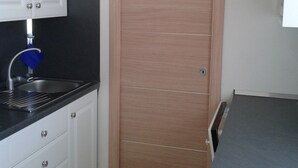 Una cocina con armarios blancos, encimera negra, un lavamanos y una puerta de madera.