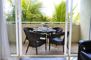 Un balcon avec une table dressée pour quatre personnes, entouré de chaises en osier, et une vue sur des palmiers.