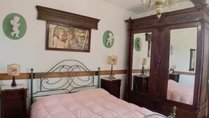 A bedroom with a bed, a wooden headboard, a chandelier, a mirror, and a framed picture on the wall.
