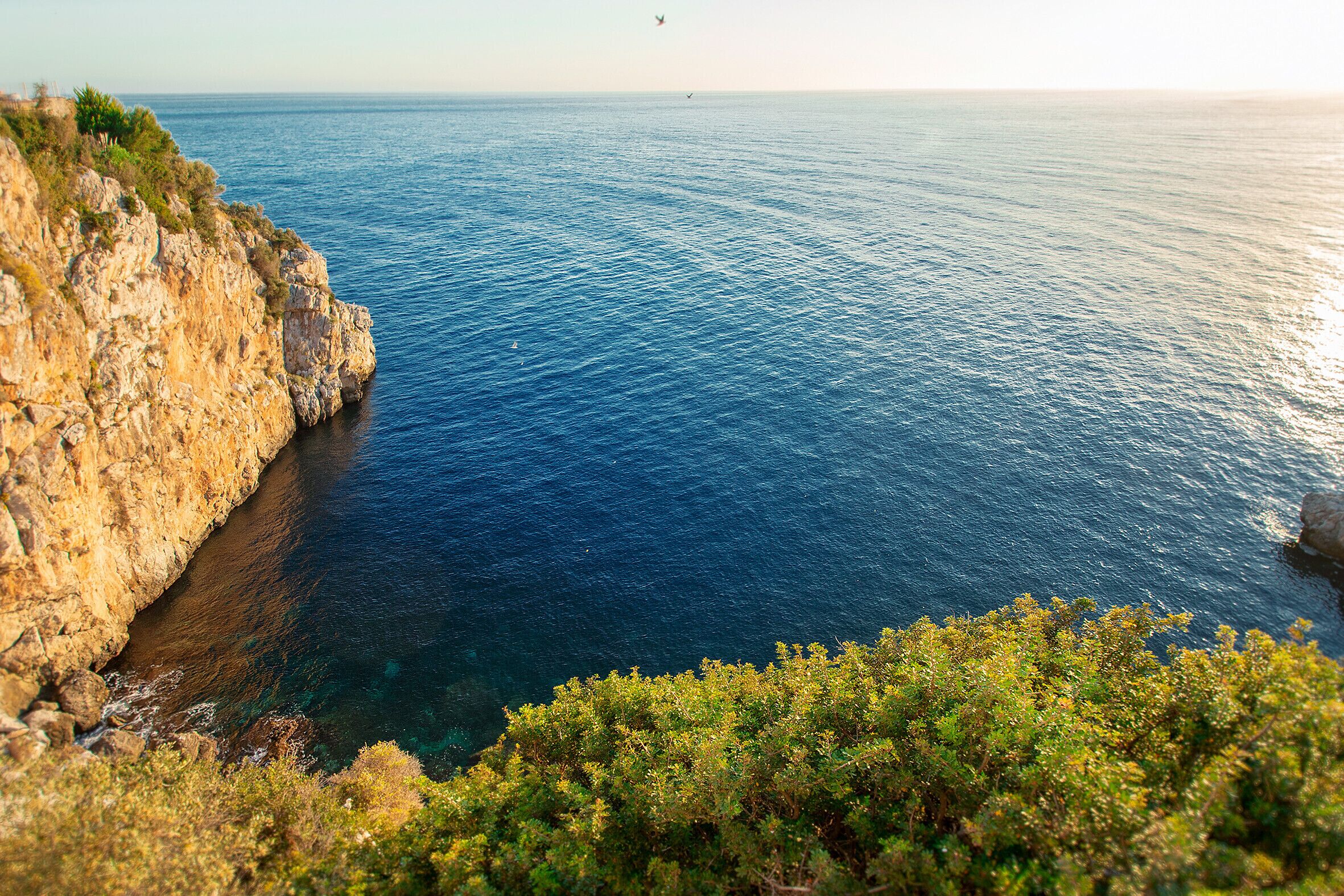A coastal landscape with a rocky cliff and clear blue sea.