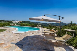 A swimming pool with stone tiles, lounge chairs, and umbrellas. - Villa Ise by Anita Villas (Montefelcino)