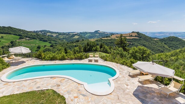 Une piscine à bord incurvé, entourée de carreaux de pierre, et dotée de mobilier d’extérieur comprenant des chaises et un parasol.
