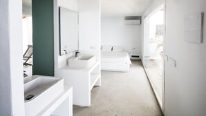 Une salle de bain moderne avec un lavabo blanc, un miroir et un lit en arrière-plan.