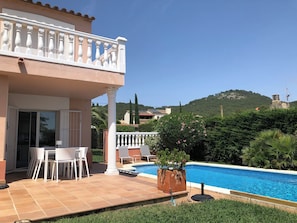 A two-story house with a balcony, a swimming pool, and a view of a hill.