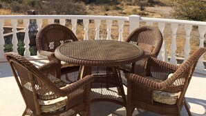 A wicker outdoor seating area with a table and chairs, overlooking a mountainous landscape.