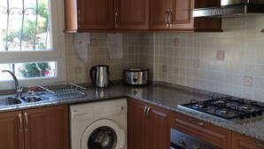 A kitchen with wooden cabinets, a washing machine, a stove, and a coffee maker.