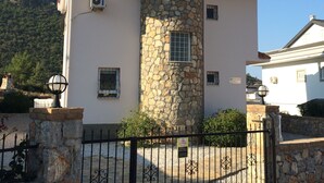 A two-story building with a stone tower, a red-tiled roof, and a gated entrance.