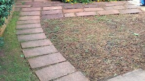Un espace extérieur abrité, doté d’une table et de chaises de patio, et entouré d’un jardin où poussent des fleurs jaunes.
