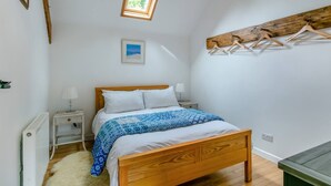 Un dormitorio con cama de madera, paredes blancas, tragaluz, mesita de noche con lámpara y banco de madera.