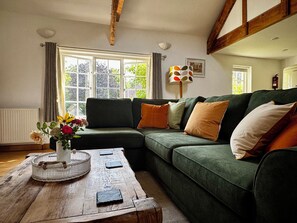 A cozy living room with a green sofa, a wooden coffee table, and a window with curtains. - Idyllic Devon Cottage Near Exeter (Crediton)