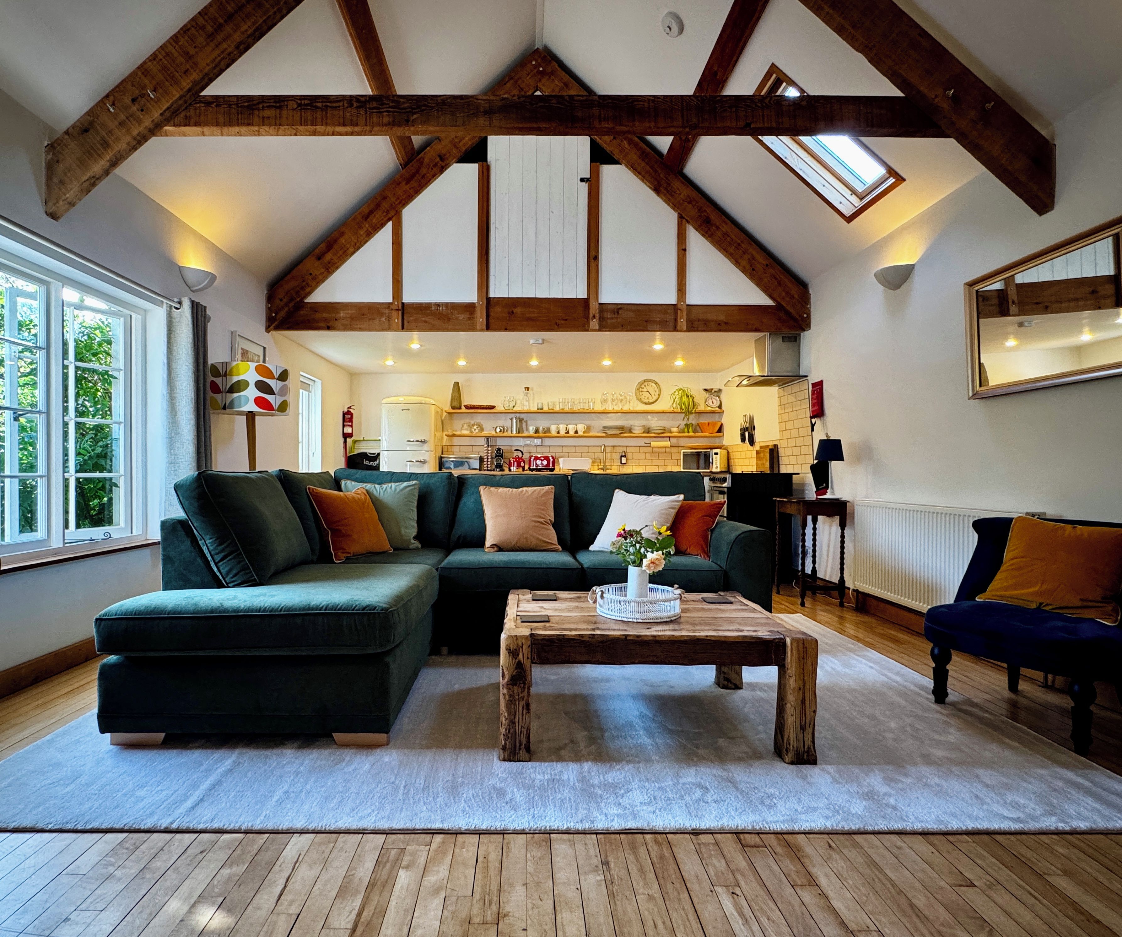 Un salon spacieux avec un grand canapé d’angle, une table basse en bois et une vue sur la cuisine grâce à un espace mezzanine ouvert.