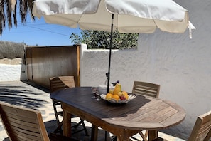 Ein Holztisch mit Stühlen, einem weißen Sonnenschirm und einer Obstschale.