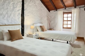 Une chambre avec deux lits, une table de chevet, une lampe, une fenêtre avec des rideaux et un plafond rustique.