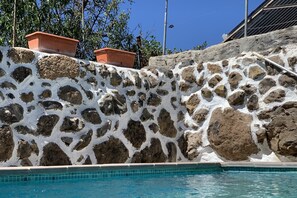 Una piscina con un muro de piedra y macetas de terracota.