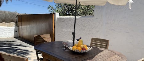 Una mesa de madera con sillas, un paraguas blanco y un frutero.