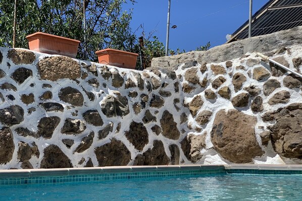 A pool with a stone wall and terracotta planters.