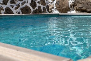 Une piscine aux eaux cristallines, bordée de carreaux et entourée d’un mur de pierres.