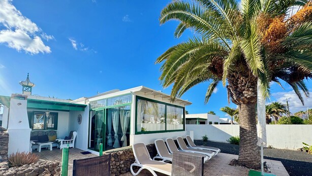 A modern outdoor seating area with a glass table and chairs, a stone wall, and a palm tree.