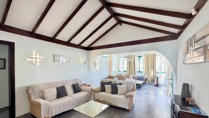 A spacious living area with a high ceiling, a sofa, a coffee table, and a dining area visible through an archway.