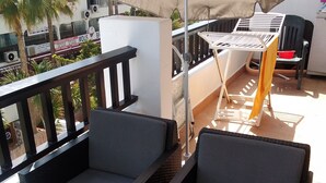 Un balcón con dos sillas oscuras de mimbre, un paraguas grande color beige y una mesa blanca.