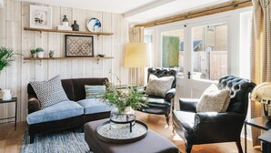A cozy living room with a dark brown sofa, a black leather armchair, and a wooden coffee table with a vase of flowers. - Boutique cottage in a quiet corner of Chipping Campden, a Cotswold gem. (Chipping Campden)