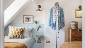 A bedroom with a sloped ceiling, a bed with patterned bedding, a hanging garment, and a bedside lamp. - Boutique cottage in a quiet corner of Chipping Campden, a Cotswold gem. (Chipping Campden)