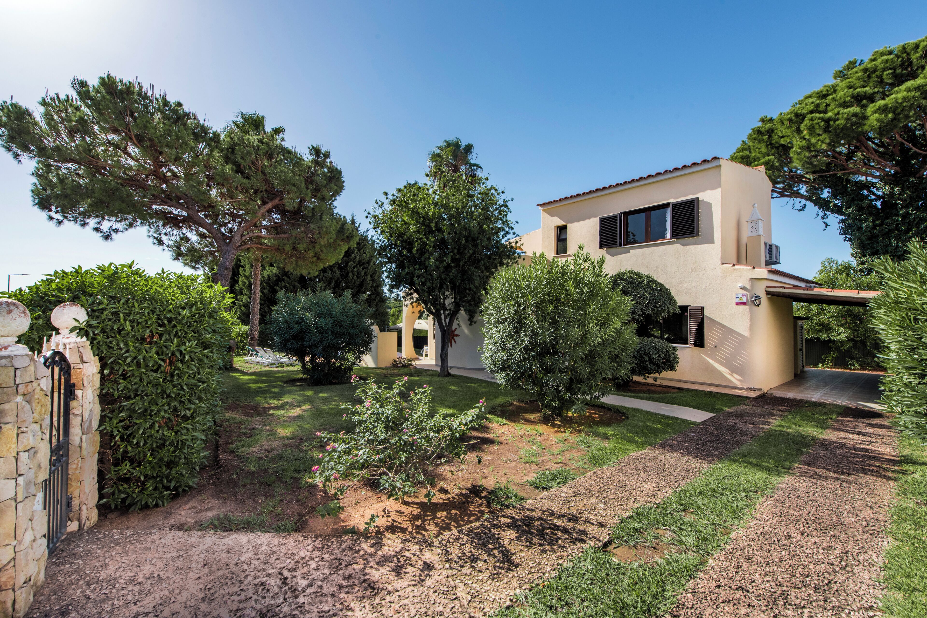 A modern two-story house with a well-maintained garden, a stone gate, and a clear sky.