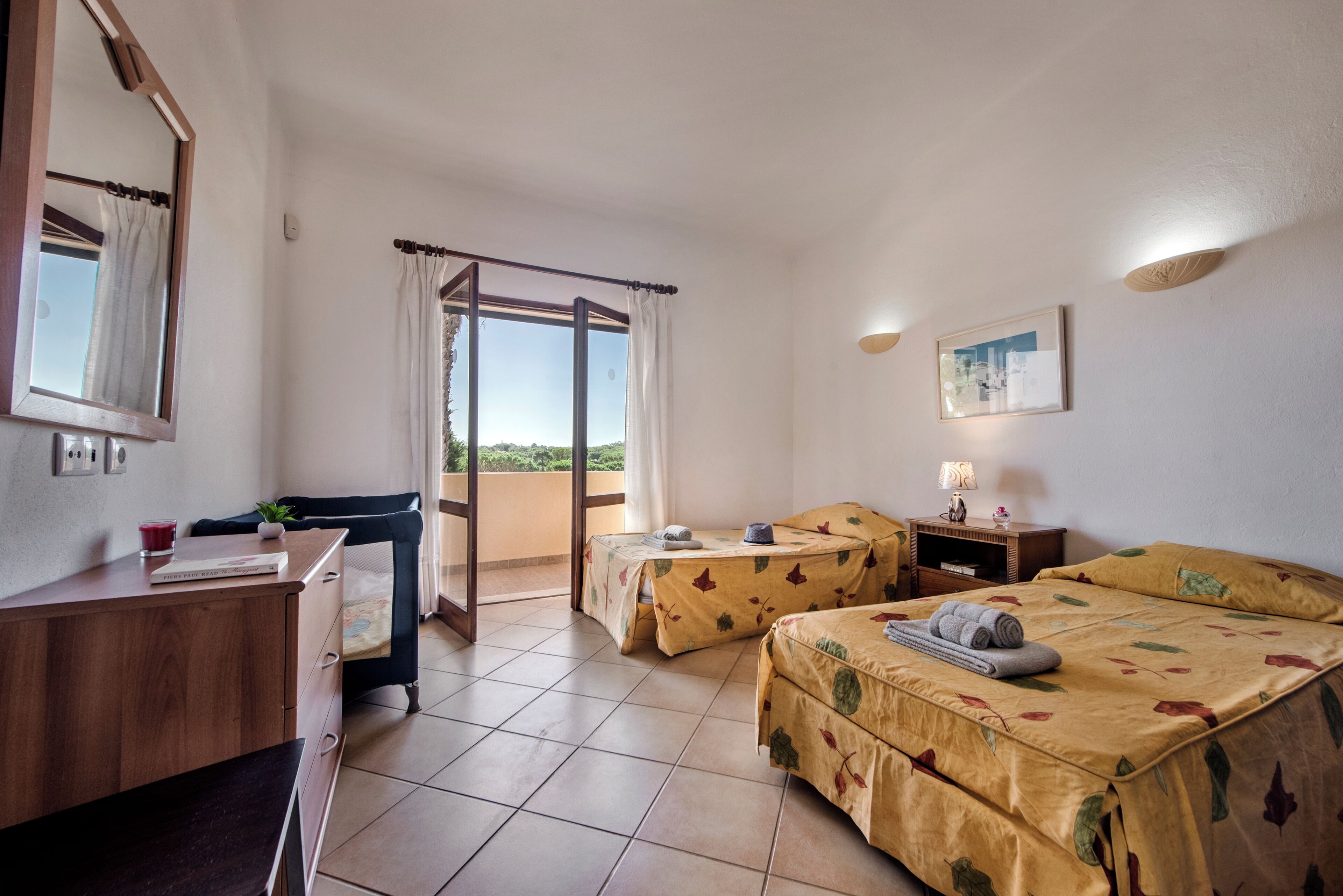 A hotel room with a desk, two beds, a balcony, and a view of the outdoors.