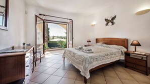 A bedroom with a bed, bedside tables, a desk, and a chair. There is a window with a view of greenery outside. - Exclusive Retreat in Vilamoura, private pool, off-street parking, Free AC & wifi (Vilamoura)