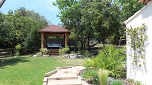 Un jardín con un pérgola de madera, un camino de piedra y diversas plantas.