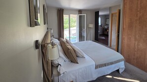 Un dormitorio con cama, mesita de noche, lámpara y vistas al baño y zona exterior.
