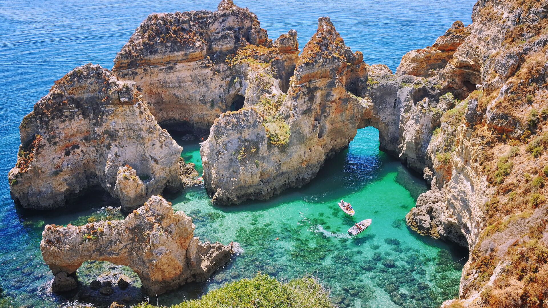 Un paysage côtier rocheux, avec une eau turquoise cristalline et un bateau.