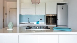 A modern kitchen with white cabinets, a stainless steel oven, a gas stove, and a blue countertop. - Villaggio S'abba e Sa Pedra - S'ABBA DI SU (Golfo Aranci)