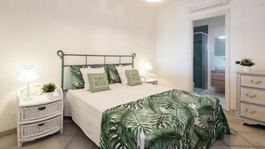 A bedroom with a bed, nightstands, a dresser, and a door leading to a bathroom. - Villaggio S'abba e Sa Pedra - S'ABBA DI SU (Golfo Aranci)