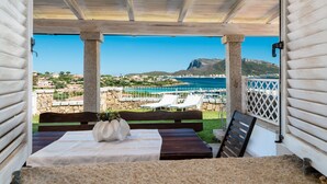 A covered outdoor seating area with a table and benches, overlooking a coastal view with a mountain and a body of water. - Villaggio S'abba e Sa Pedra - S'ABBA DI SU (Golfo Aranci)