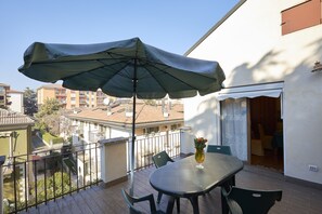 Ein Balkon mit Tisch und Stühlen, einem grünen Sonnenschirm und einem Blumenvasen.
