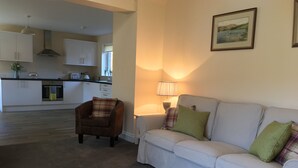 Ein Wohnzimmer mit einem weißen Sofa, einem braunen Sessel, einer Lampe und einer Küche im Hintergrund.
