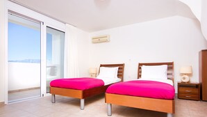 Camera d'albergo con due letti, una porta scorrevole in vetro che dà su un balcone, un piccolo comodino con una lampada e un condizionatore d'aria a parete.