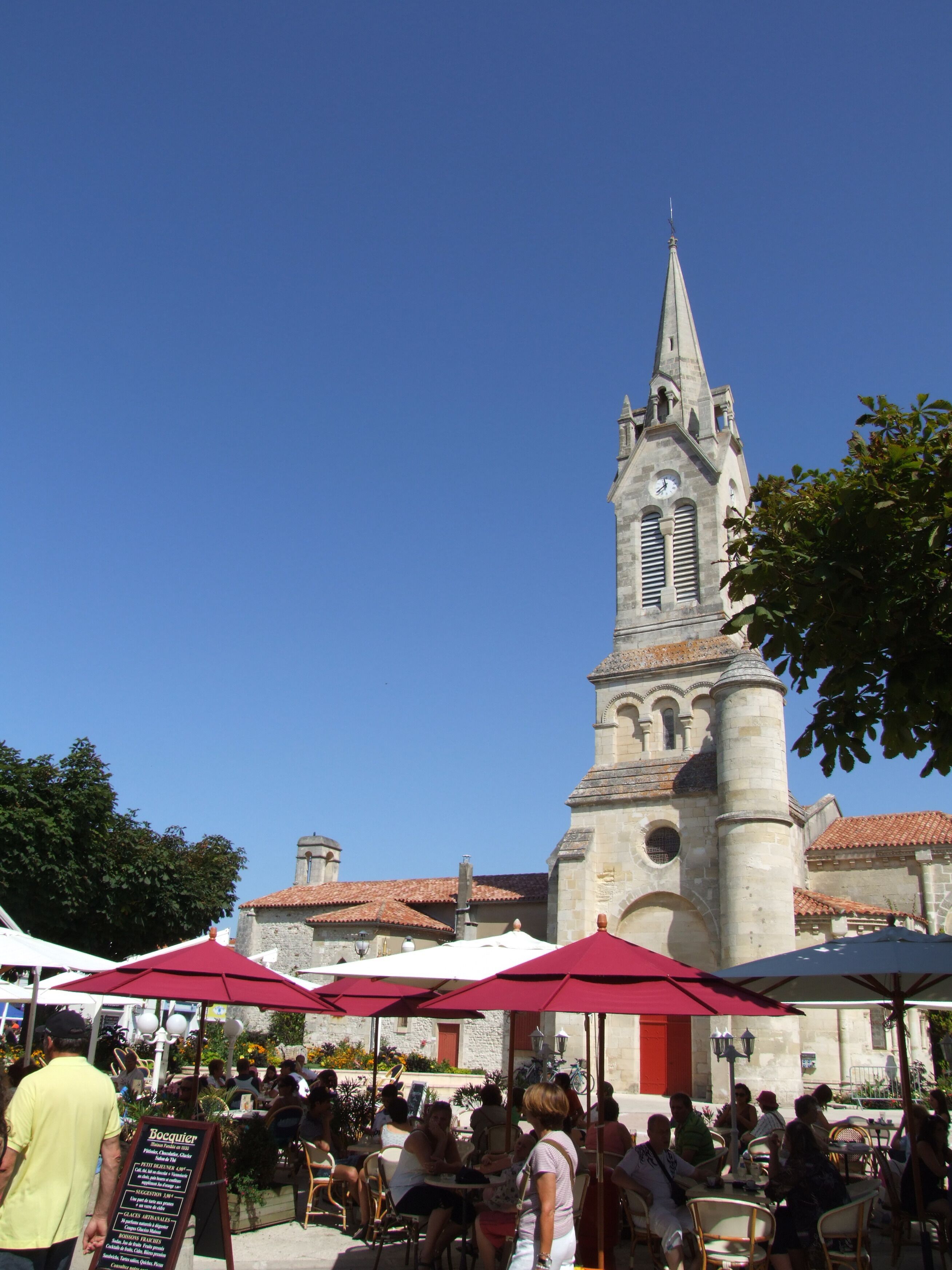A historic church with a tall bell tower and a courtyard with outdoor seating.
