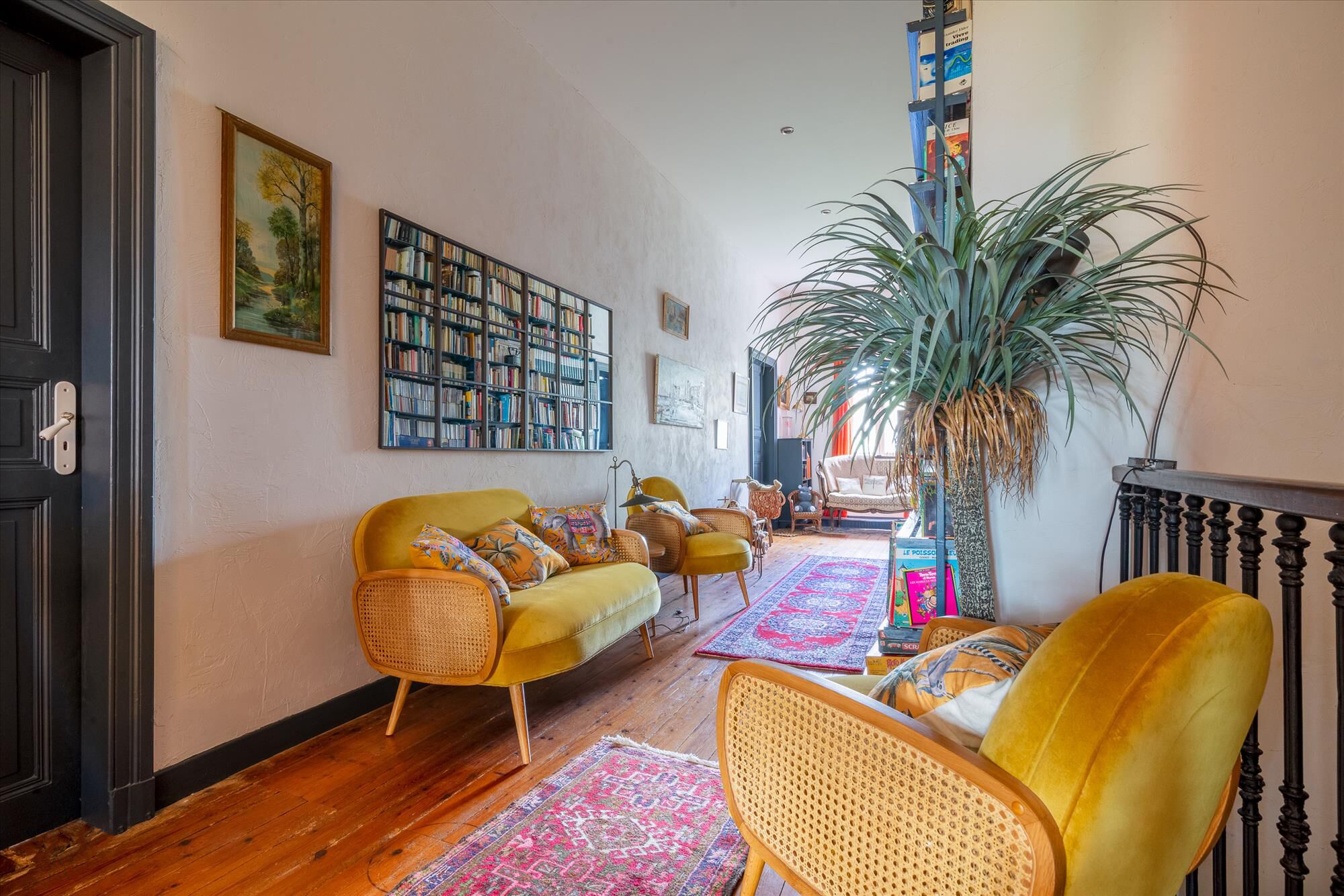 Un salon chaleureux avec une bibliothèque, une grande plante et un canapé jaune.