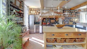 A kitchen with wooden shelves, hanging pots, and a central island with baskets. - Beautiful house with swimming pool, in Little Tuscany between Albi and Toulouse (Ambres)