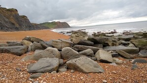 A rocky beach with large boulders and pebbles, a cliff in the background, and the ocean. - Characterful 18th century cottage in Bridport close to the Jurassic Coast. (Bridport)