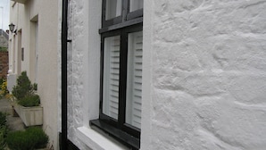 A white building with a window featuring white shutters and a black frame. - Characterful 18th century cottage in Bridport close to the Jurassic Coast. (Bridport)