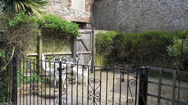 A stone building with a brick section, surrounded by a gravel path and a metal fence. - Characterful 18th century cottage in Bridport close to the Jurassic Coast. (Bridport)