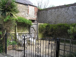 A stone building with a brick section, surrounded by a gravel path and a metal fence. - Characterful 18th century cottage in Bridport close to the Jurassic Coast. (Bridport)