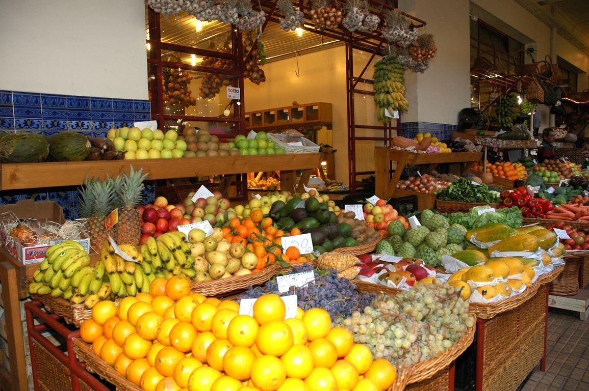 Un étal de marché proposant une variété de fruits et de légumes, notamment des bananes, des pommes, des oranges et des raisins.